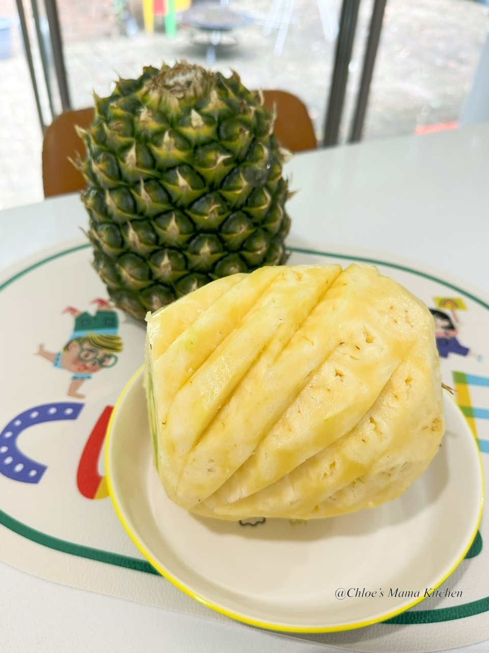 A peeled fresh pineapple on a plate beside an unpeeled pineapple