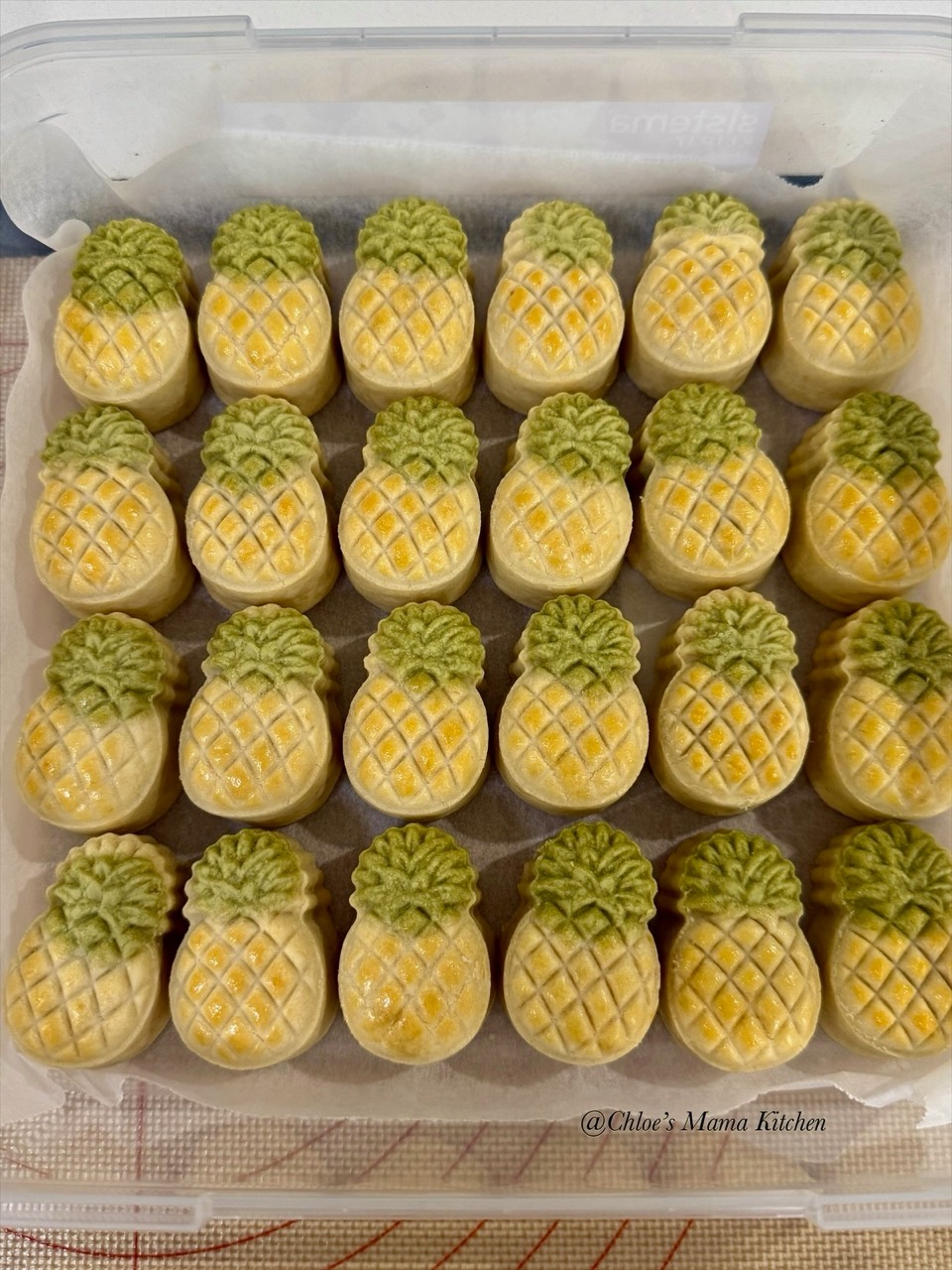 Rows of golden pineapple tarts with green leaves in a lined container