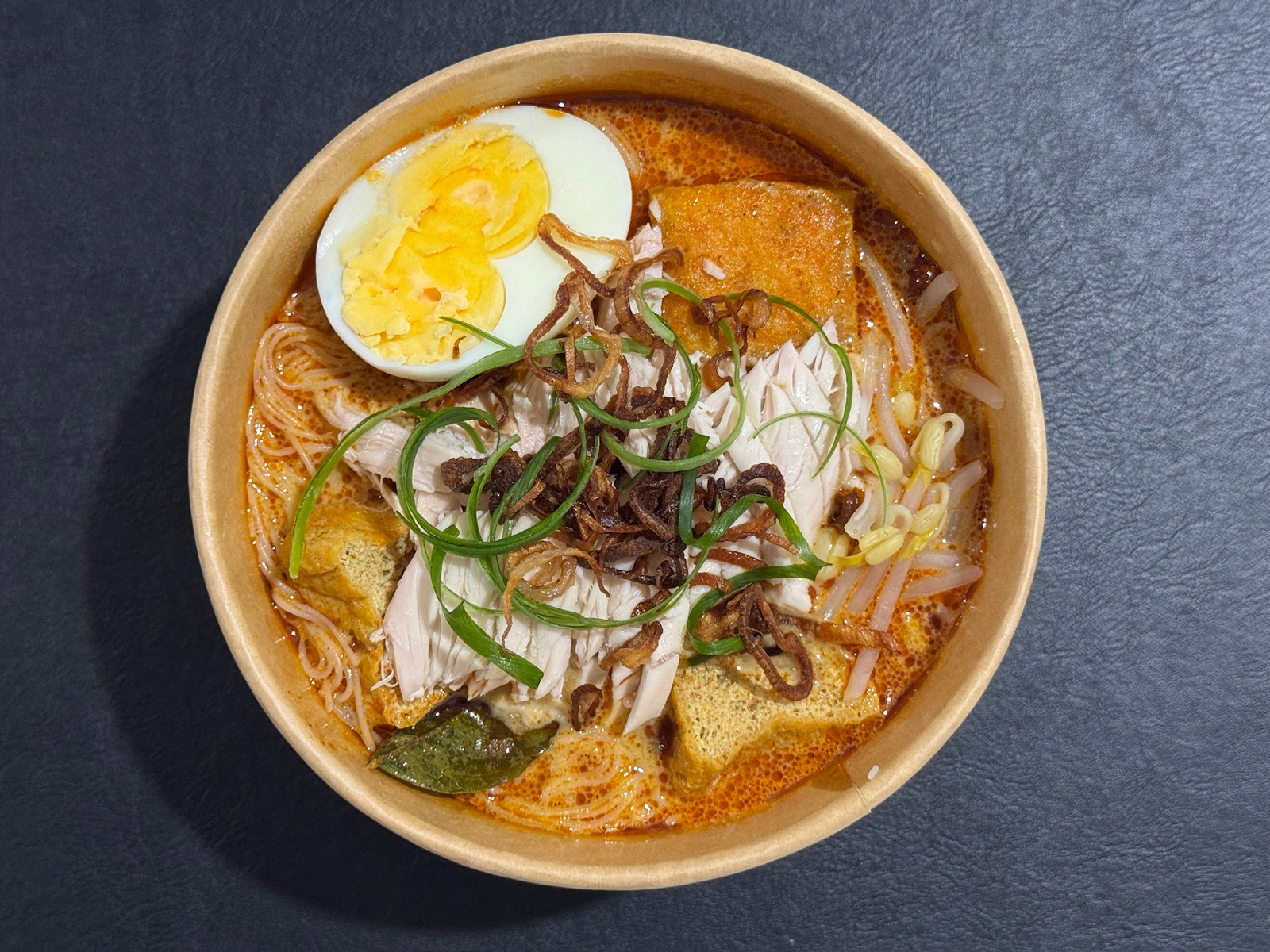 Chicken laksa with chicken, noodles, tofu puffs and egg in a bowl.