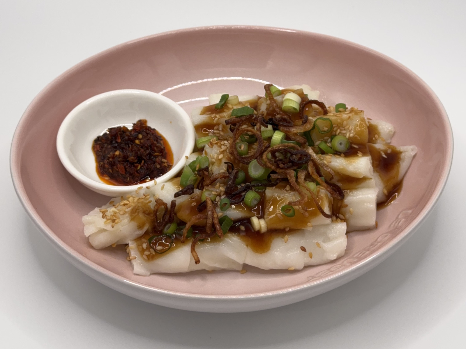 Handmade Malaysian-style Chee Cheong Fun on a pink plate, with sambal on the side.