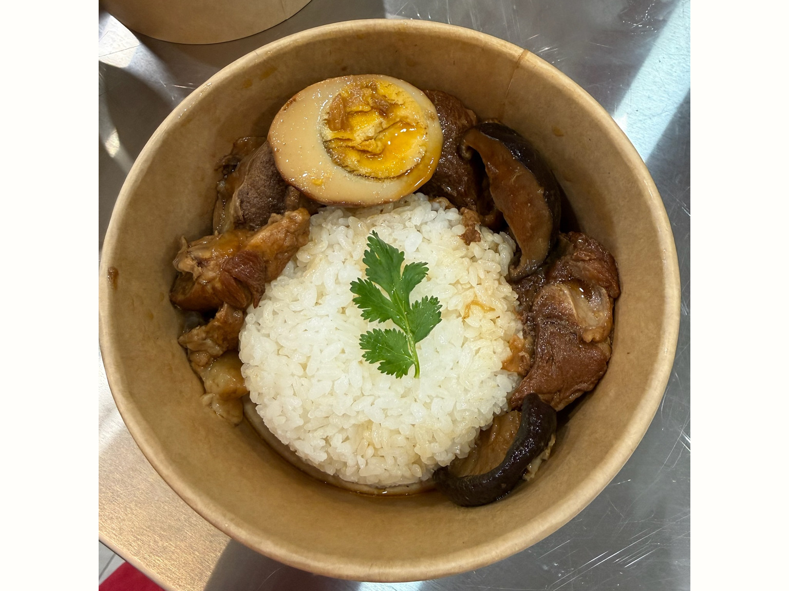 Braised pork knuckle rice in a paper bowl, with rice, braised pork, mushrooms and egg. The foreground bowl is the subject; a neighbouring bowl is in the background.